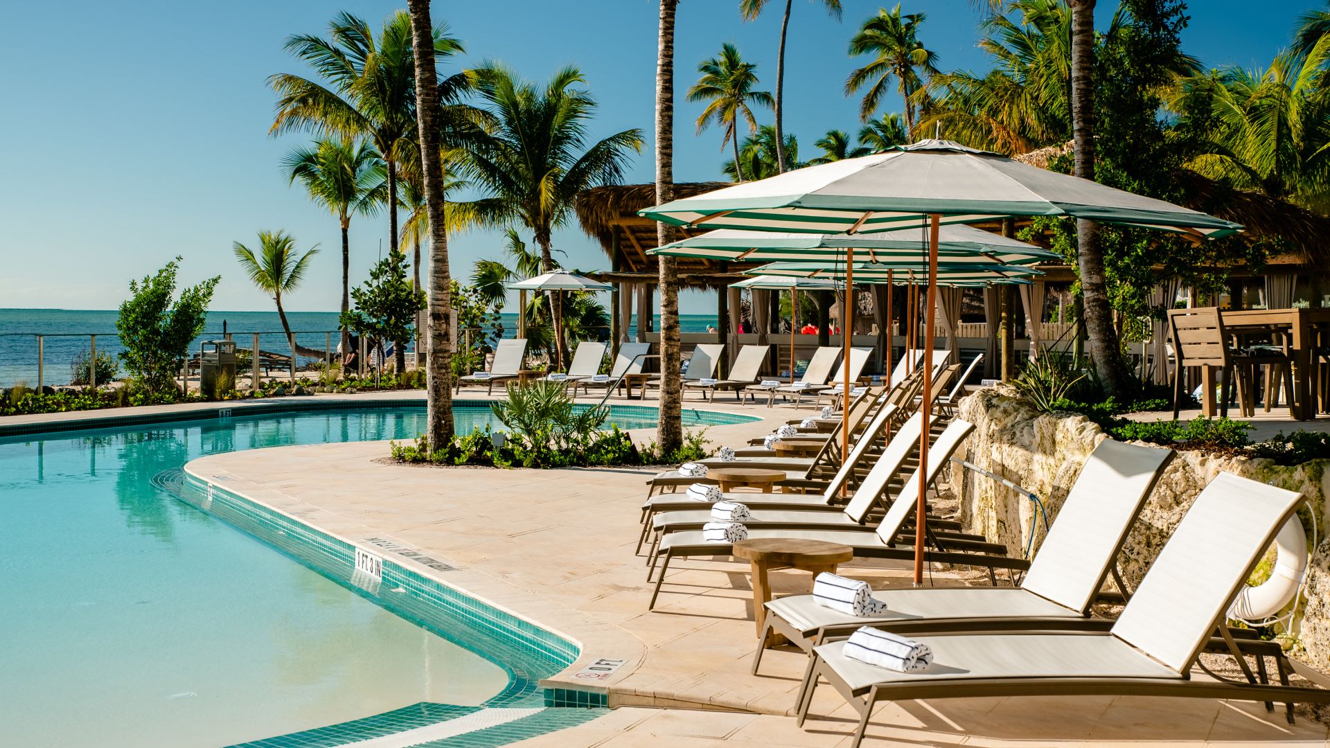 A Pool With Lounge Chairs And Umbrellas By A Beach
