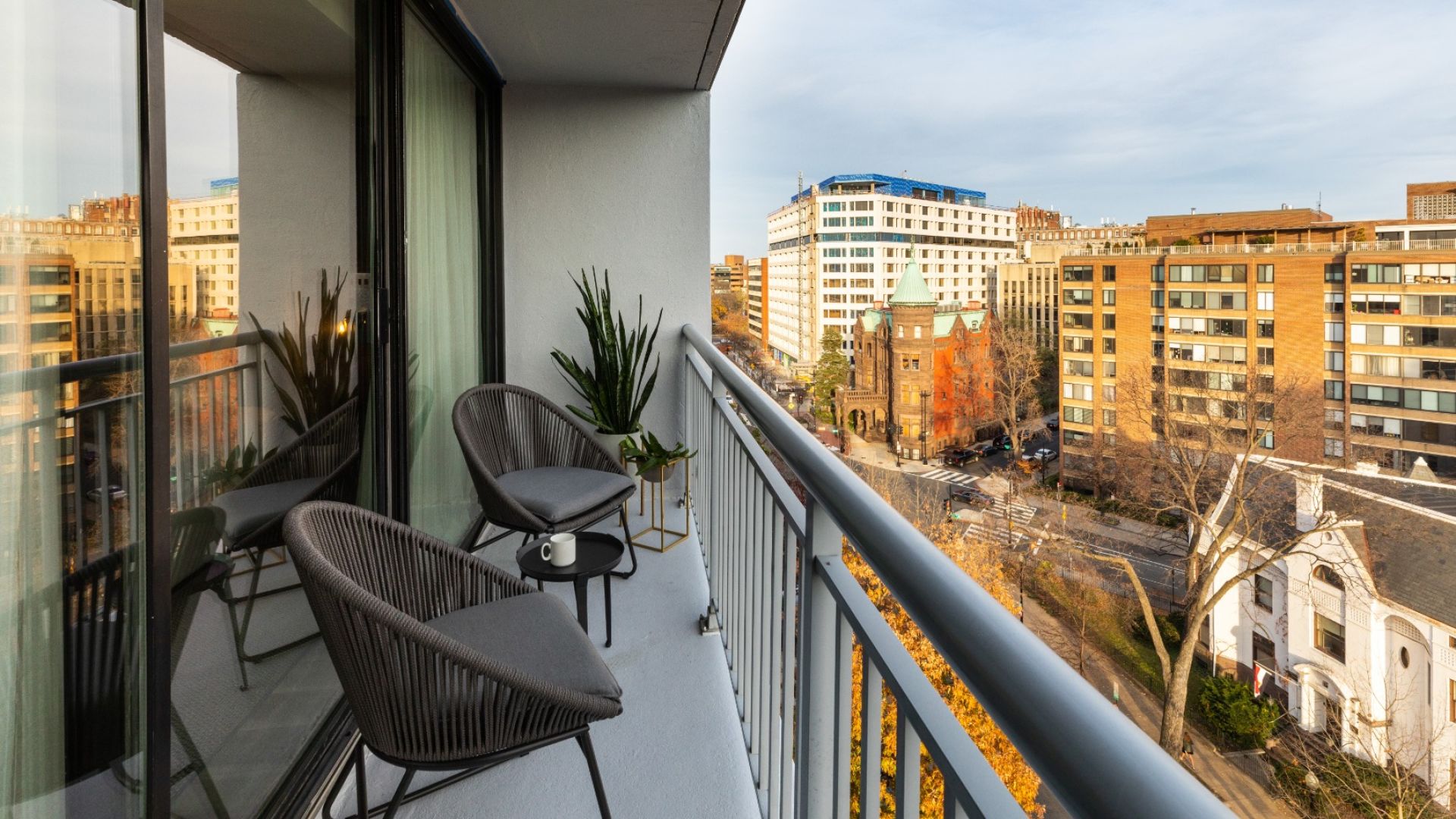 A Balcony With A View Of A City And A Patio With Chairs And Tables And Plants