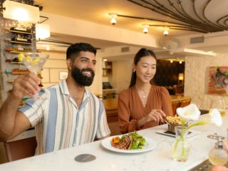 A Man And Woman Sitting At A Table With Food And Drinks