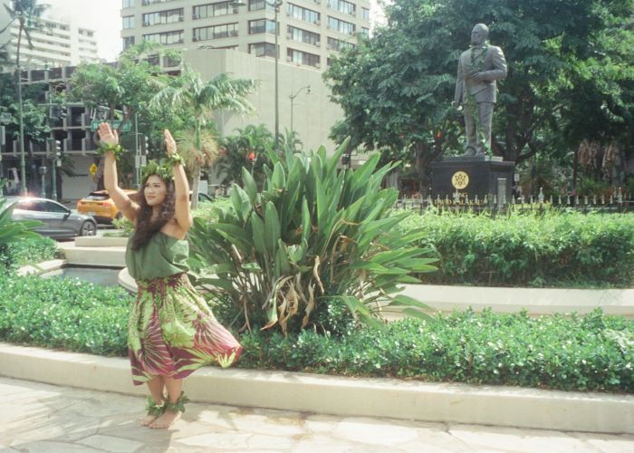 A Person In A Dress Holding A Tree In Front Of A Statue