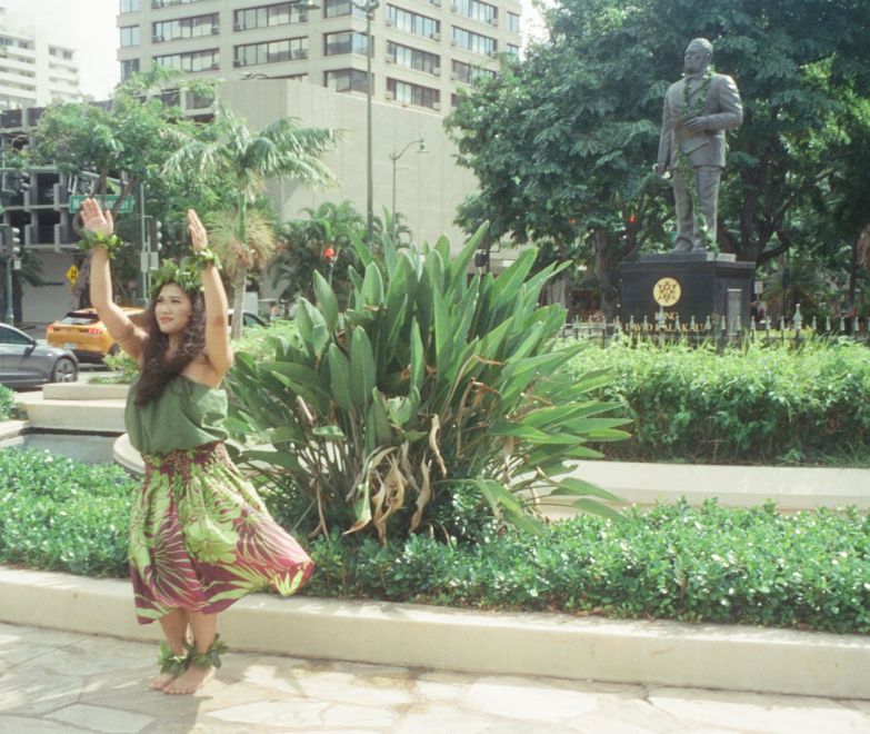 A Person In A Dress Holding A Tree In Front Of A Statue
