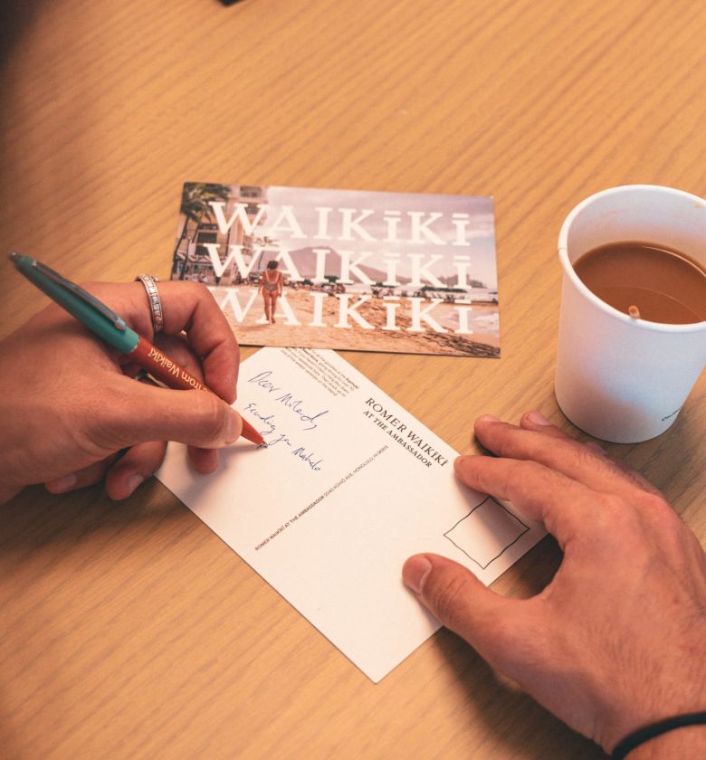 A Person Writing On A Piece Of Paper Next To A Cup Of Coffee