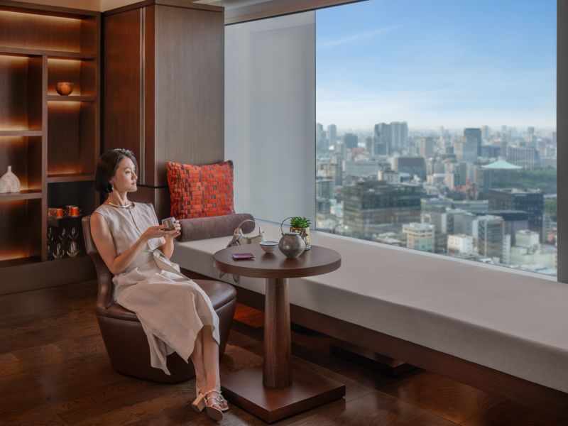 A Person Sitting On A Chair In Front Of A Window Overlooking A City