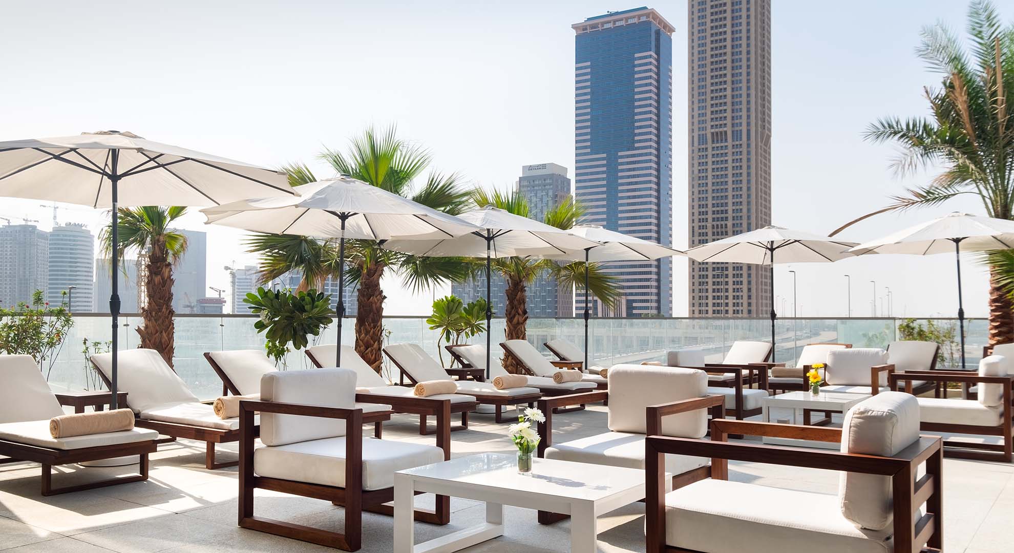 A Patio With Lounge Chairs And Umbrellas With Tall Buildings In The Background