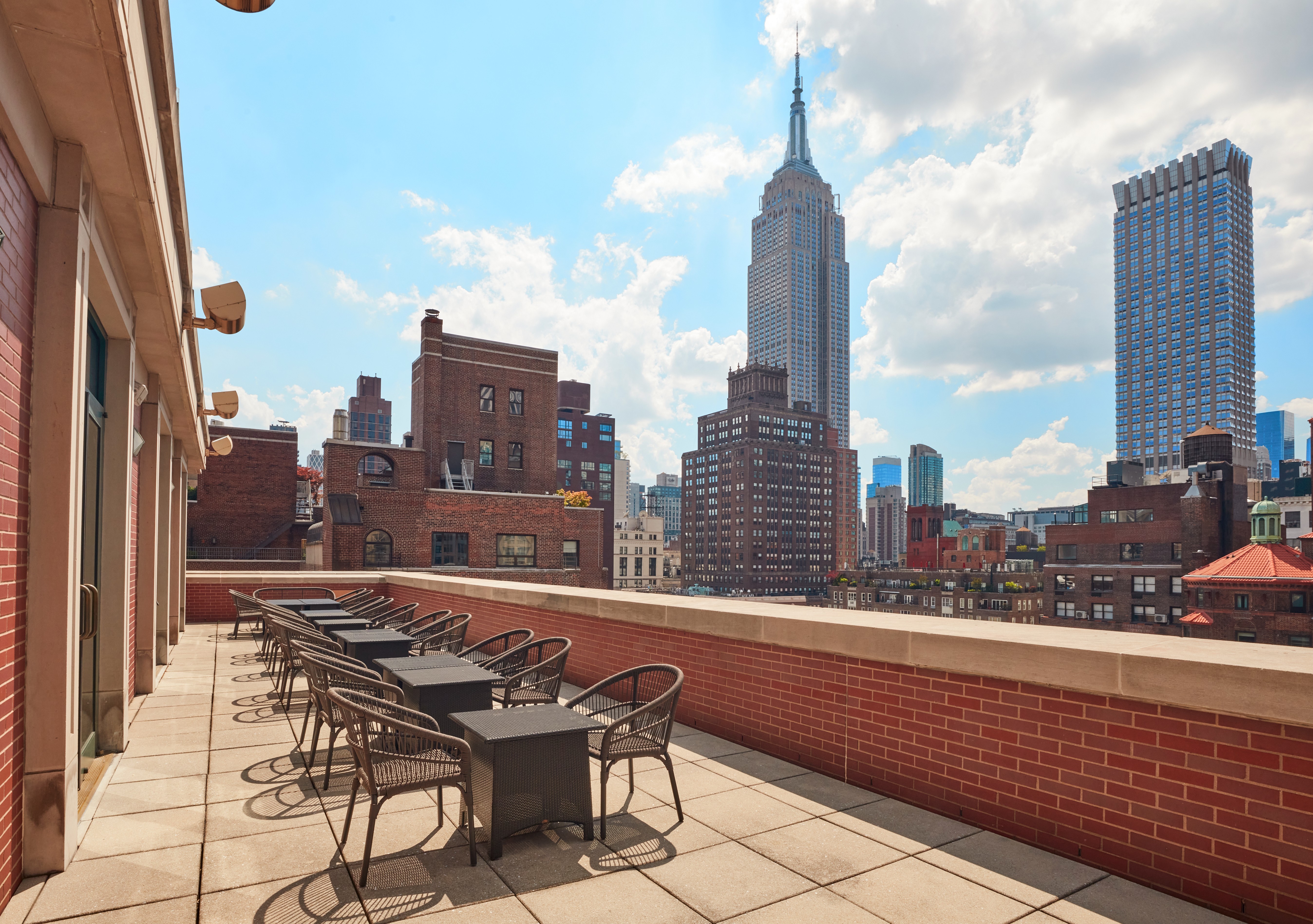 A Brick Patio With Tables And Chairs And A Brick Wall With A City Skyline In The Background